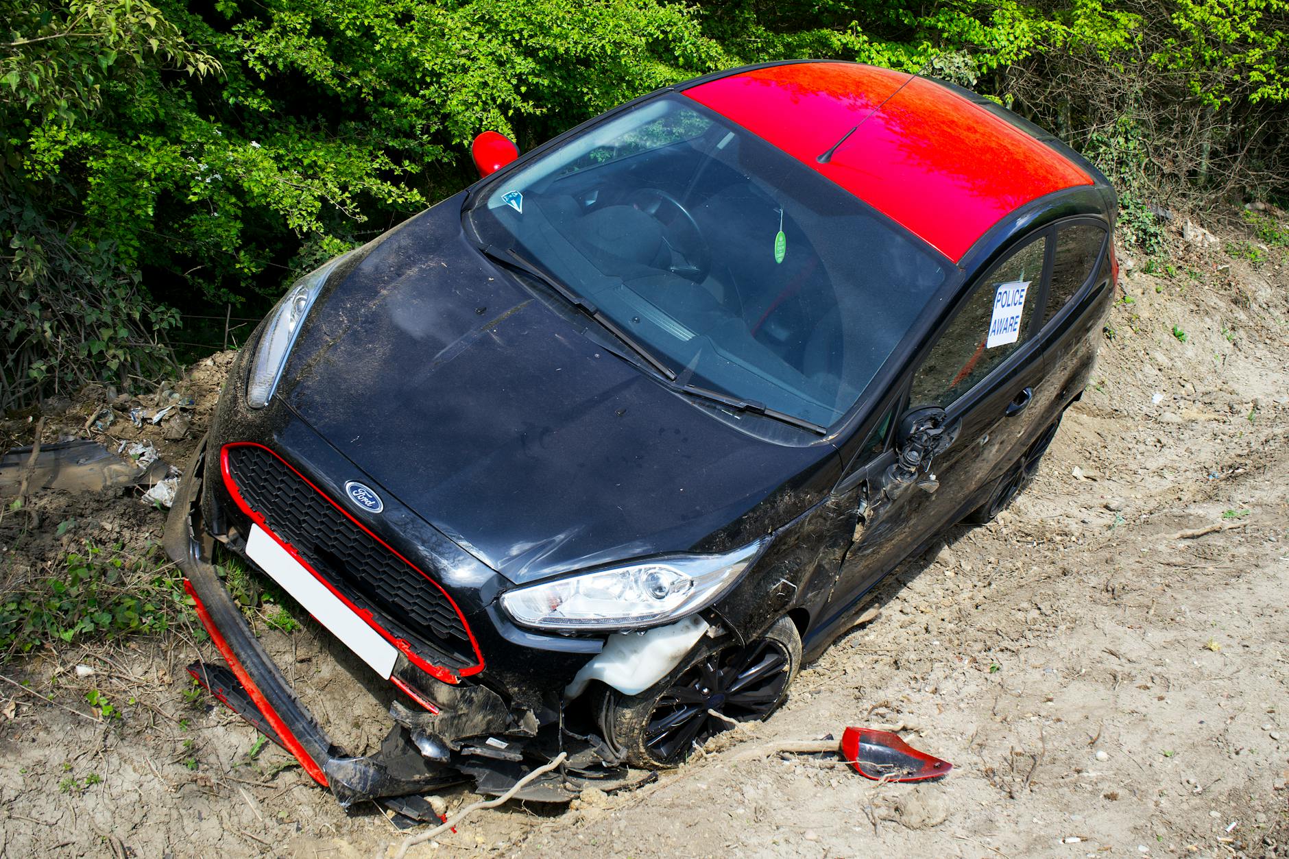 Uszkodzony czarno-czerwony Ford Fiesta stojący poza drogą