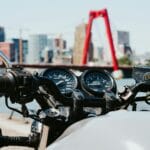 Strefa Tempo 30 a motocykl: czy zasady są inne niż dla aut? Kierownica motocykla w mieście na tle czerwonego mostu