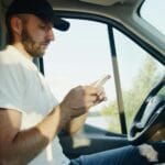 Jak kupić winietę online bez wpadki: Austria, Czechy, Słowacja, Szwajcaria Mężczyzna w zaparkowanym aucie kupuje winietę na smartfonie