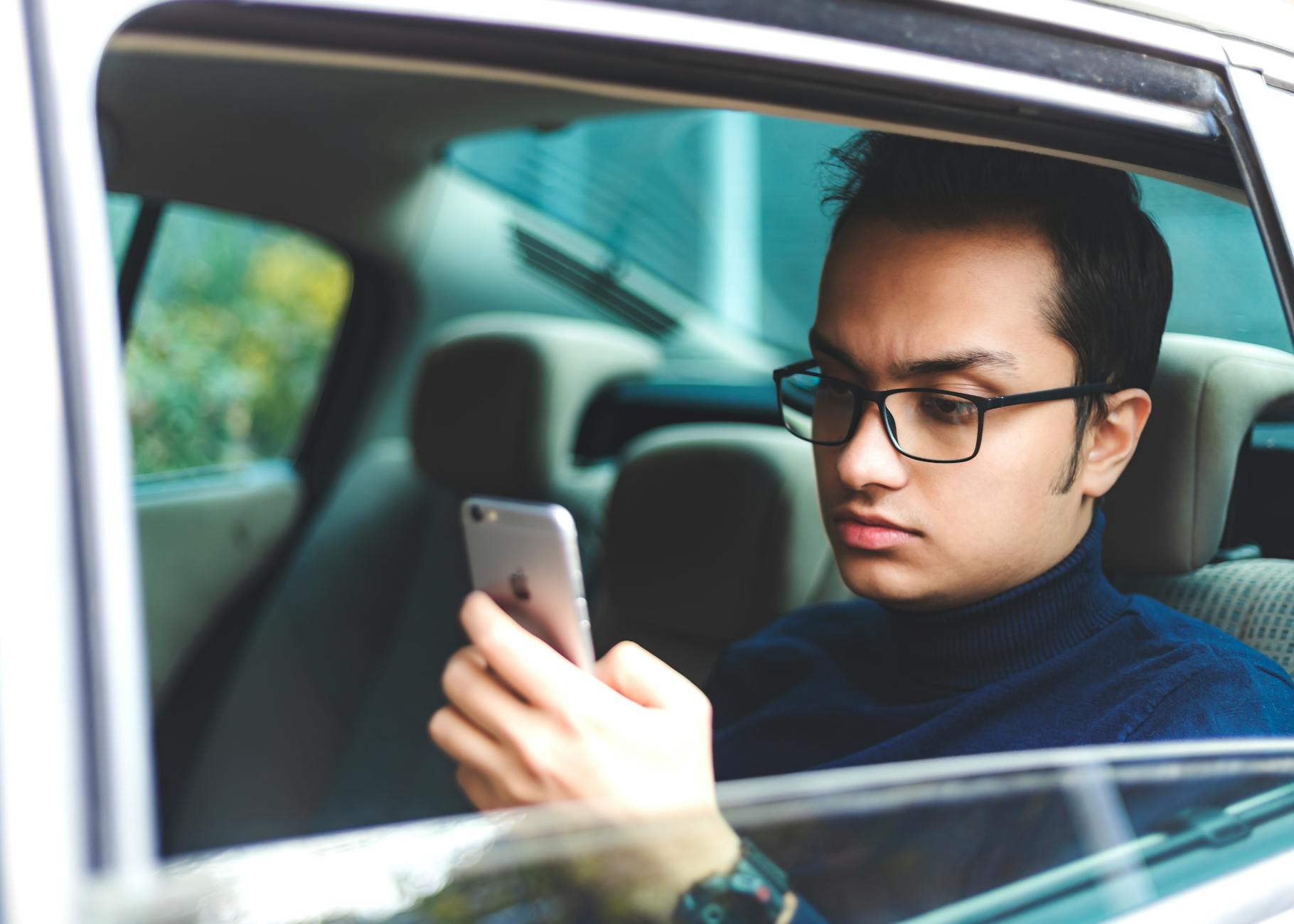 Młody mężczyzna w okularach korzysta z telefonu w zaparkowanym aucie